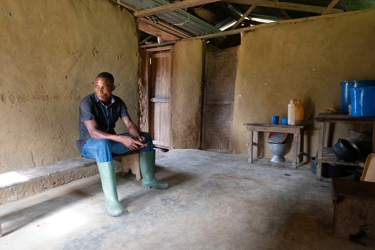 Man in wellies sitting on a wooden bench in his house in Gbolobo in Liberia 